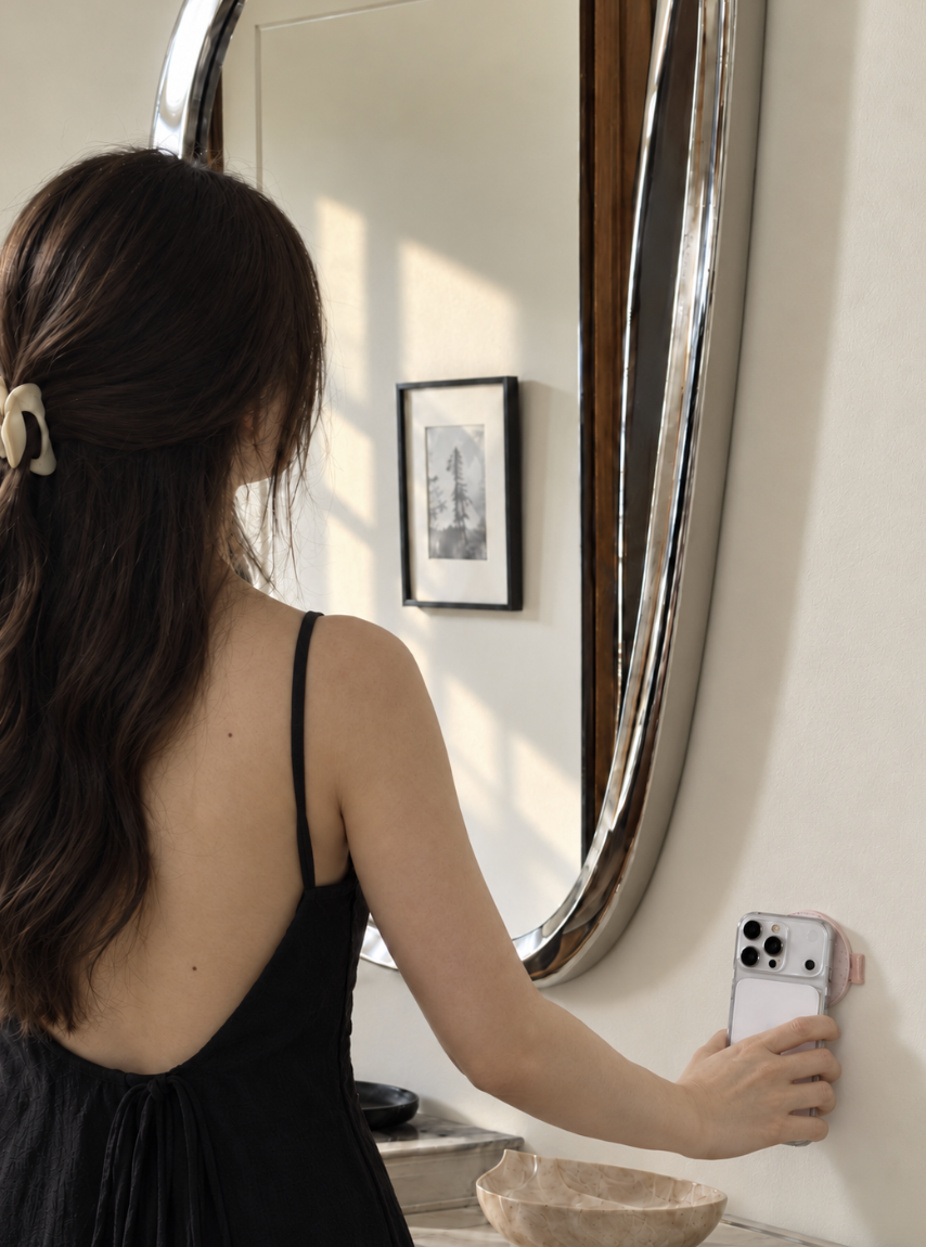 A woman tapping her phone to a small habit sticker on the wall beside a mirror.